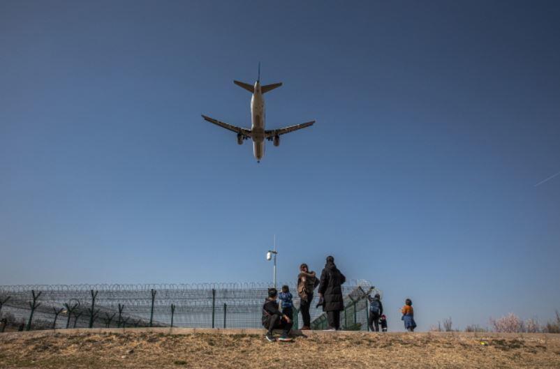 Ludzie stojący w parku patrzą na samolot lądujący na międzynarodowym lotnisku w stolicy, w Pekinie, w Chinach, 17 marca 2020 / autor: PAP/EPA/ROMAN PILIPEY