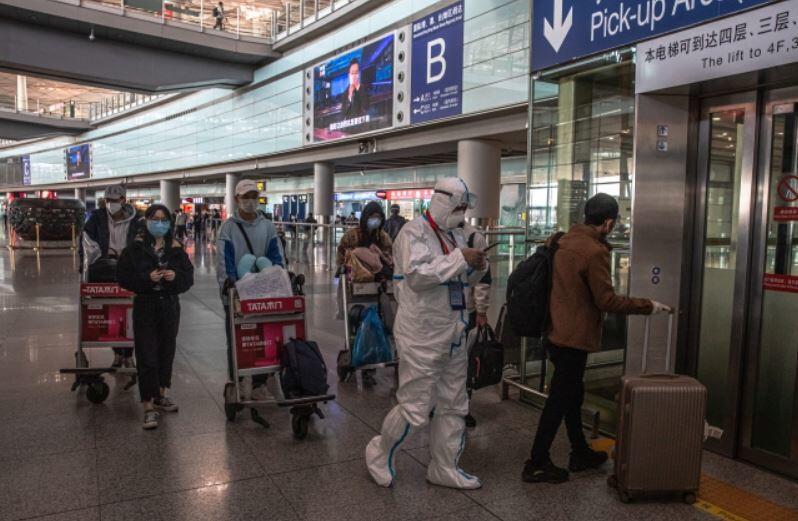 Podróżujący w maskach ochronnych podążają za pracownikiem w pełnym stroju ochronnym w strefie przylotów na międzynarodowym lotnisku w stolicy, w Pekinie, Chiny, 17 marca 2020 r. / autor: PAP/EPA/ROMAN PILIPEY