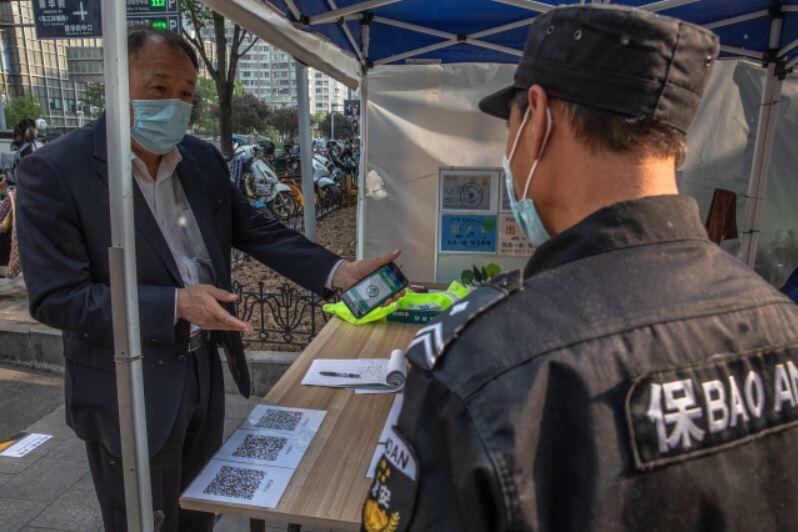 Mężczyzna w ochronnej masce na twarzy pokazuje swój zielony kod przy wejściu bezpieczeństwa do dzielnicy mieszkalnej i biurowej w Pekinie, / autor: PAP/EPA/ROMAN PILIPEY