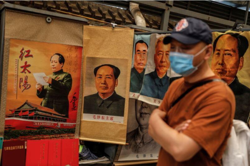 Mężczyzna w masce obok stoiska sprzedającego portrety byłego chińskiego przywódcy Mao Zedonga na targu antyków Panjiayuan w Pekinie Chiny, 23 maja / autor: PAP/EPA/WU HONG